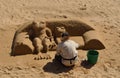 :Woman making sand sculpture of Frog sitting on sofa on Cascais beach.