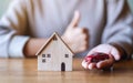 A woman making and showing thumbs up hand sign while holding car figure model and wooden house model Royalty Free Stock Photo