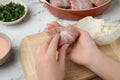 Woman making stuffed cabbage roll at white table, closeup