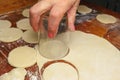 Woman making ukrainian dumplings or varenyky, cutting with a glass the round pieces of dough