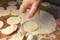 Woman making ukrainian dumplings or varenyky, cutting with a glass the round pieces of dough