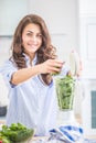 Woman making vegetable soup or smoothies with blender in her kitchen. Young happy woman preparing healthy drink with spinach