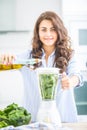 Woman making vegetable soup or smoothies with blender in her kitchen. Young happy woman preparing healthy food or drink with olive