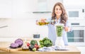 Woman making vegetable soup or smoothies with blender in her kitchen. Young happy woman preparing healthy food or drink with olive Royalty Free Stock Photo