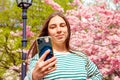 woman making video call, taking selfie portrait with mobile phone. Young smiling european white female woman on on cherry blossom Royalty Free Stock Photo