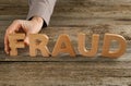 Woman making word Fraud with wooden letters at table, closeup