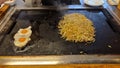 woman is making yakisoba on a hot stove where water, raw ingredients and eggs are placed on a hot plate