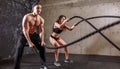 Woman and man couple training together doing battling rope workout