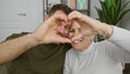 A woman and a man form a heart shape with their hands, showcasing affection in a light indoor setting Royalty Free Stock Photo