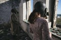 A woman and man in a gas mask stands in an abandoned building and looks out the window