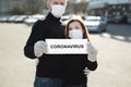 A woman and a man in protective medical masks hold a placard reading coronavirus. Message for prevention of bovine