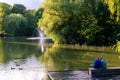 A woman and a man sitting on a wooden bench by a pond in the park Stadsparken in Lund, Sweden