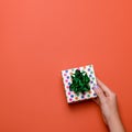 Woman manicured hands holding green gift box on dark orange background, copy space, top view, flat lay. Giving presents or Royalty Free Stock Photo