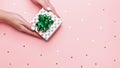 Woman manicured hands holding green giftbox on pastel pink background with confetti, copy space, top view, flat lay. Giving Royalty Free Stock Photo