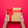 Woman manicured hands holding red and golden wrapped present or gift box on deep red background, copy space, top view, flat lay.