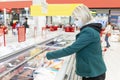 A woman with a mask on examining a frozen good in the refridgerated goods area at a supermarket. Shopping during the pandemic.