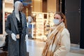 Woman in mask face next to clothing mannequin in shopping mall. Living with the coronavirus pandemic