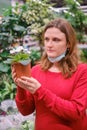 A woman with a mask looks at white violets in a flowerpot. Growing flowers and plants at home during corona virus isolation