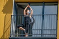 Woman in mask practices yoga on balcony of