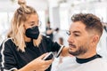 Woman with mask shaving a man with an electric machine in a barbershop Royalty Free Stock Photo