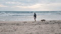 A woman with mask walking along kuta beach bali with her dog at sunset