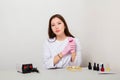 Woman is a master of nails, in a white coat and gloves, sitting at a table with spread manicure tools