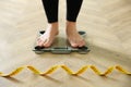 Woman with measuring tape standing on scales indoors, closeup. Overweight problem