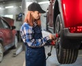 Woman mechanic uses pneumatic wrench to tighten the wheel nut. Girl at men& x27;s work. Royalty Free Stock Photo