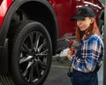 Woman mechanic uses pneumatic wrench to tighten the wheel nut. Girl at men's work. Royalty Free Stock Photo