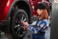 Woman mechanic uses pneumatic wrench to tighten the wheel nut. Girl at men's work. Royalty Free Stock Photo