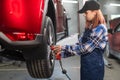 Woman mechanic uses pneumatic wrench to tighten the wheel nut. Girl at men& x27;s work. Royalty Free Stock Photo