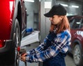 Woman mechanic uses pneumatic wrench to tighten the wheel nut. Girl at men's work. Royalty Free Stock Photo