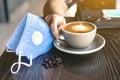 Woman with medical face mask drinking coffee in her house alone during corona virus or COVID-19 quarantine, Physical distancing