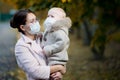 Woman in a medical face mask holds a crying baby girl in her arms