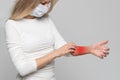 Woman in medical face mask scratching arm colored in red, on grey background. Symptoms of animal allergy, itchy skin