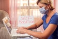 Woman with medical face mask working with laptop at home. Paper with title