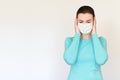 A woman in a medical mask grabbed her head in her hands and looks down. Shot on a white background.