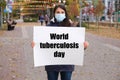 A woman in a medical mask holds a poster with the text World tuberculosis day