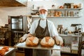 Woman with medical mask holds tray with freshly baked breads in craft workshop