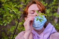A woman in a medical mask in spring near a tree with green leaves. Concept of ending the coronavirus epidemic and recovering from
