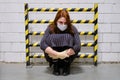 A woman in a medical mask is standing in a dead end near a yellow-and-black-striped security fence, concept Royalty Free Stock Photo