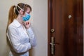 A woman in a medical mask stands in front of the front door. Self-isolation to prevent the COVID-19 coronavirus pandemic
