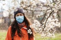 A woman in a medical mask stands on the street near a flowering tree. Concept of seasonal pollen Allergy and viral infections Royalty Free Stock Photo