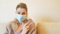 Woman in medical mask with thermometer in hand at home