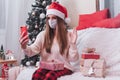 Woman in mask with Christmas gift having a video call call on mobile phone Royalty Free Stock Photo