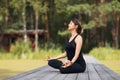 A woman meditates in a lotus position on a wooden walkway on a summer sunny morning