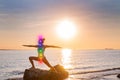 Woman is meditating with glowing seven chakras on the beach. Silhouette of woman is practicing yoga at sunset on stone