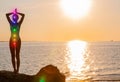 Woman is meditating with glowing seven chakras on the beach. Silhouette of woman is practicing yoga at sunset