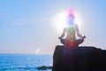 Woman is meditating with glowing seven chakras on stone at sunset. Silhouette of woman is practicing yoga on the beach