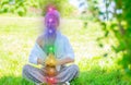 Woman is meditating in the lotus pose with glowing seven chakras on grass. Woman is practicing yoga on the park Royalty Free Stock Photo